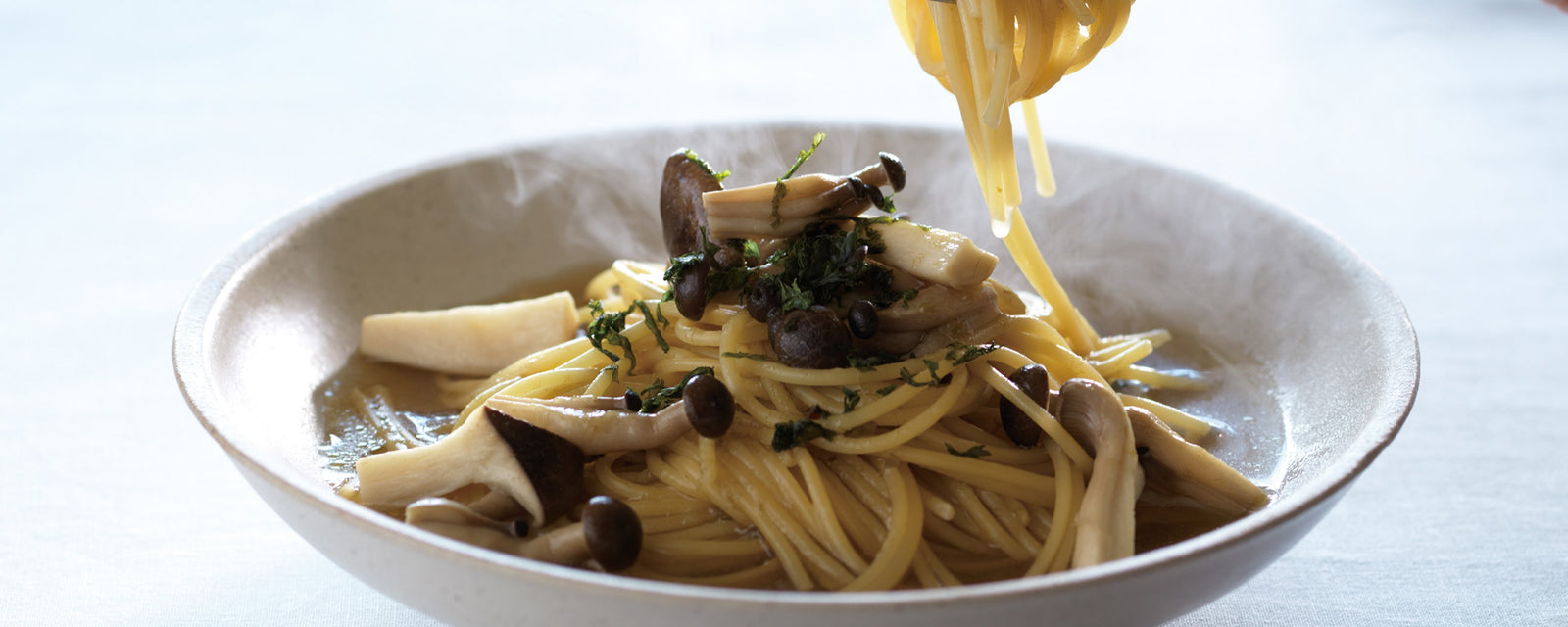 Spaghetti in light umami dashi broth with mixed mushrooms, with noodles being lifted from the bowl