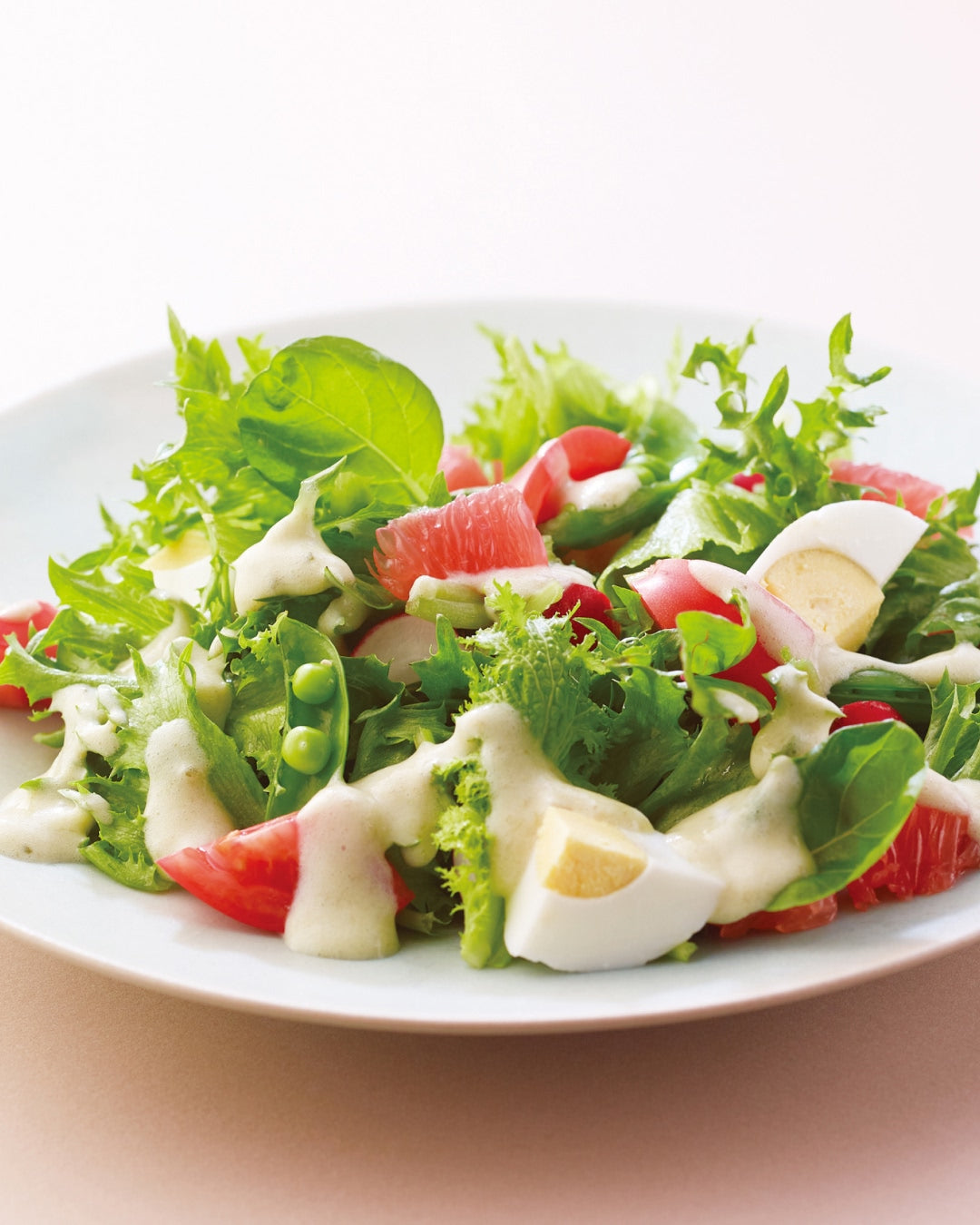 Green salad with grapefruit, boiled egg, and creamy dressing on a white plate
