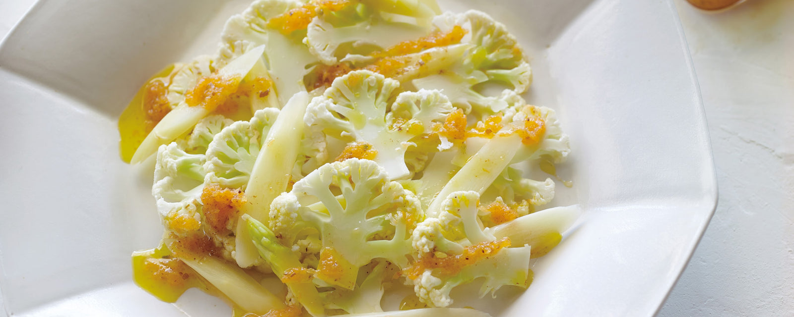 Cauliflower and white asparagus salad with carrot dressing on a white plate
