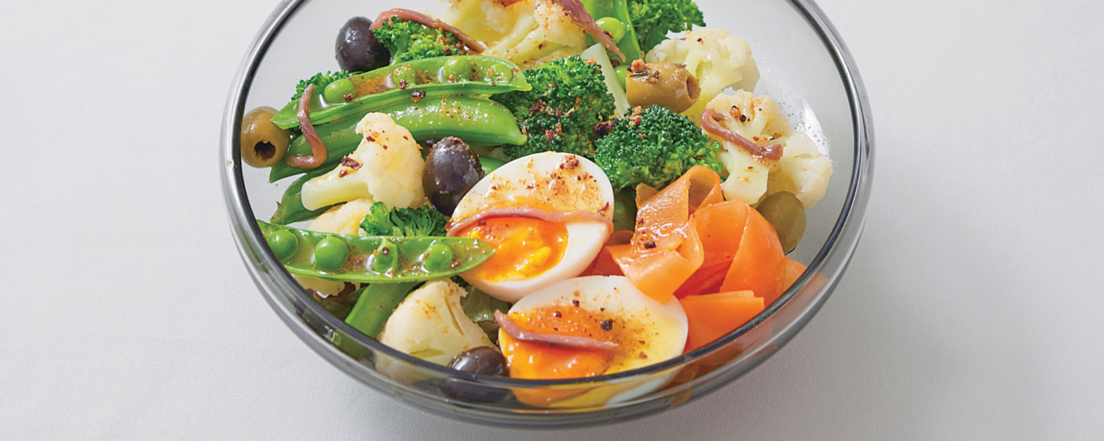 Mixed vegetable salad with soft-boiled egg, olives, and anchovies in a glass bowl