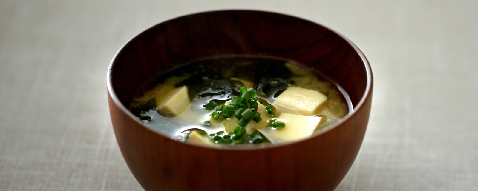 Miso soup with tofu, wakame seaweed, and chopped green onions in a wooden bowl