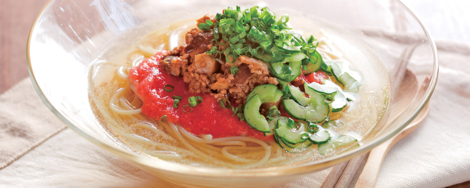 Chilled noodle soup with minced meat, mushroom, tomato, cucumber, and green onions in a clear broth