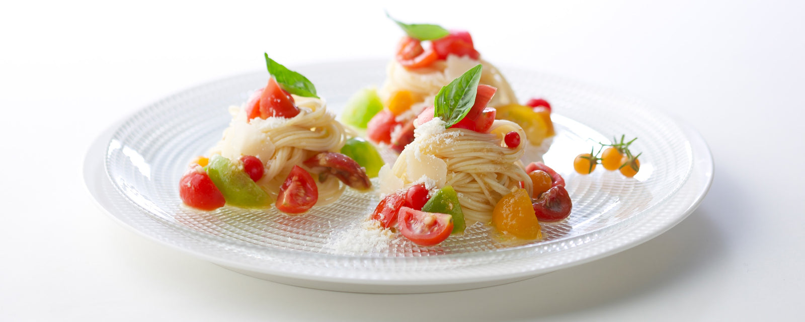Caprese-style cold pasta with cherry tomatoes, basil, and grated cheese arranged on a plate
