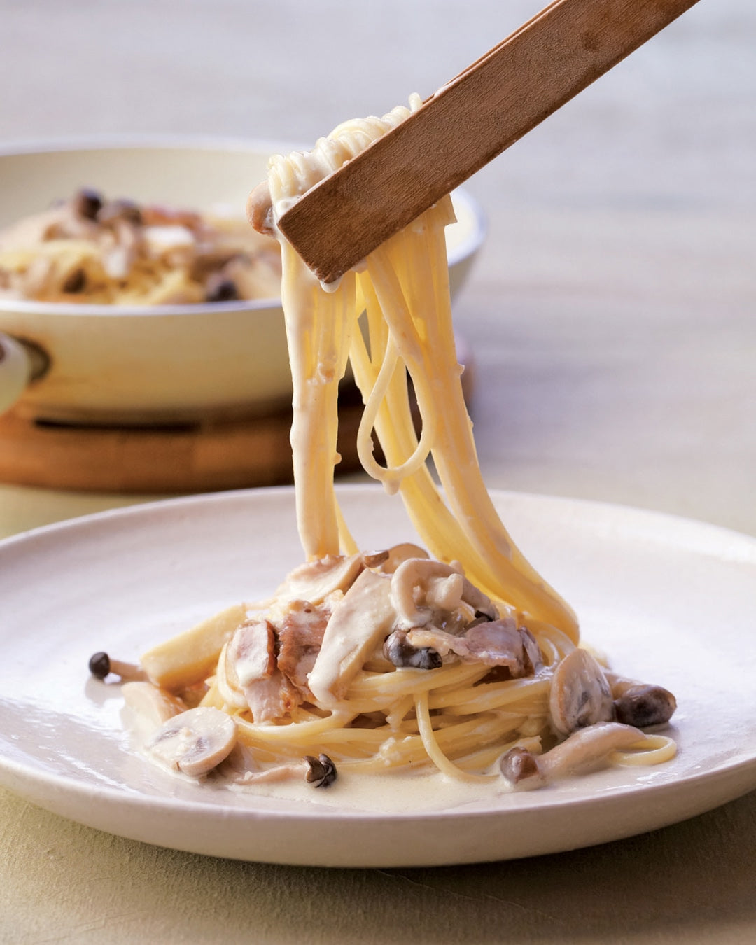 Creamy mushroom pasta with bacon being lifted from a plate