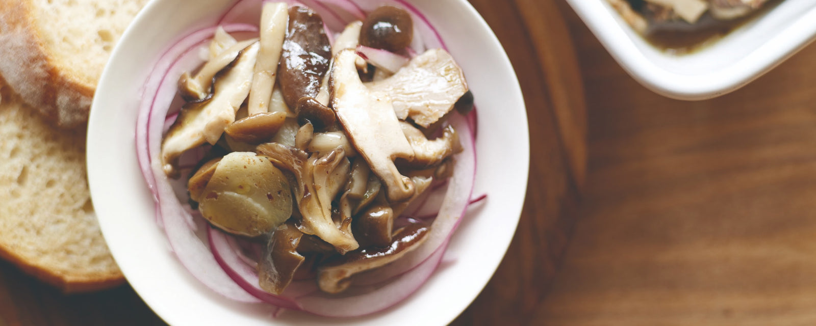 Marinated mushrooms and red onion salad served in a small bowl with bread