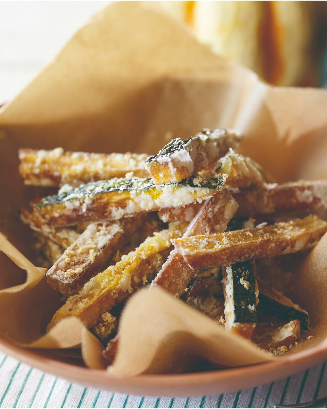 Crispy fried pumpkin sticks coated with cheese powder in a paper-lined bowl.