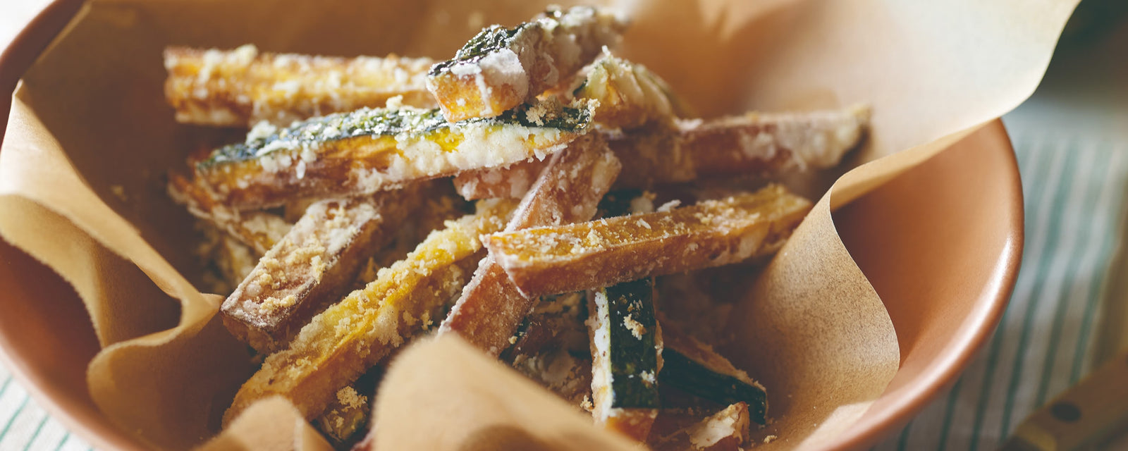 Crispy fried pumpkin sticks coated with cheese powder in a paper-lined bowl.