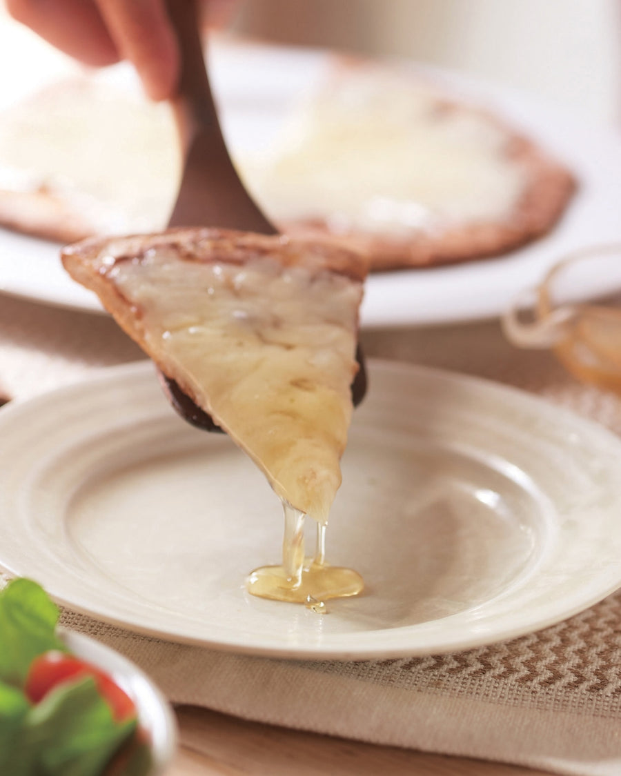 A slice of honey-drizzled pizza being served over a plate.