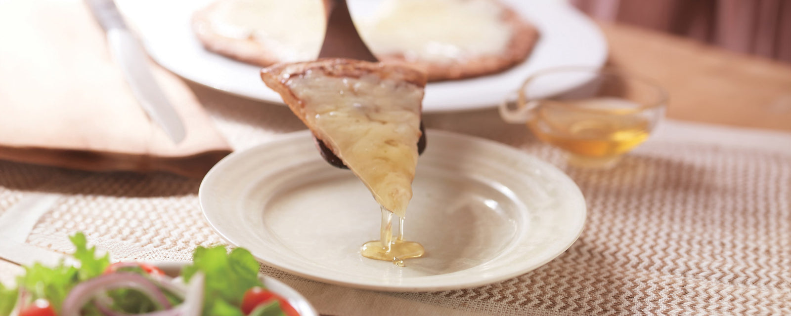 A slice of honey-drizzled pizza being served over a plate.