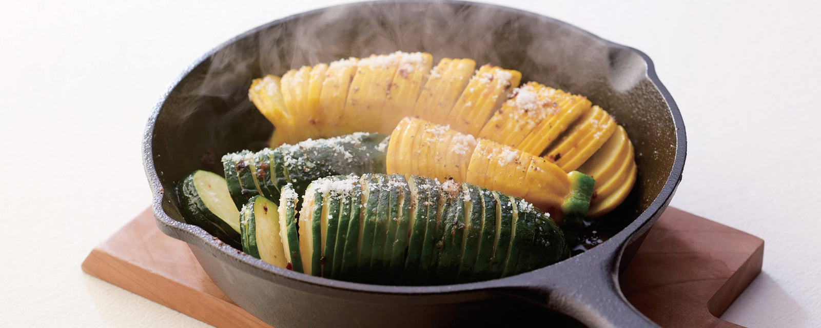 Hasselback-style yellow and green zucchini baked in a skillet with seasoning.