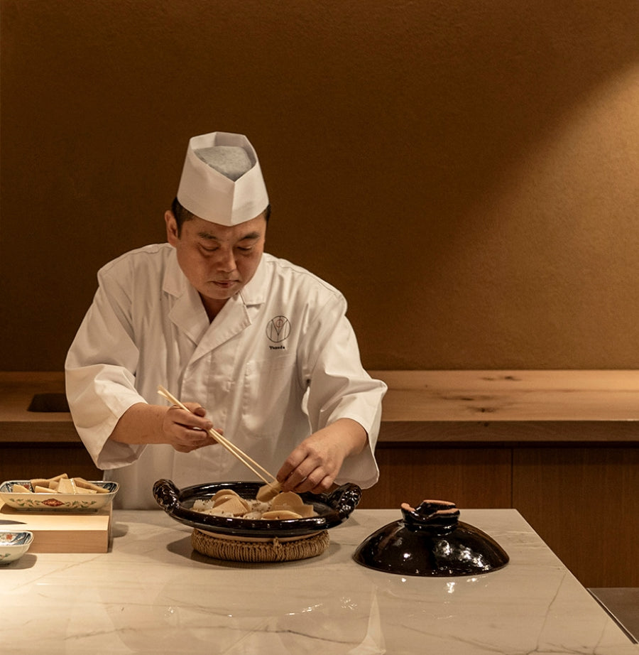 Chef in a traditional white uniform and hat preparing food in a kitchen.