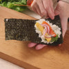 Rolling rice and fillings in nori to make cone-shaped hand roll sushi